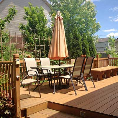 Home deck area with chairs, a table, and some trees behind it
