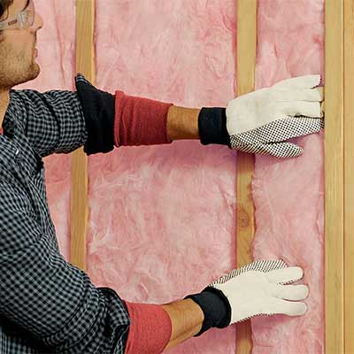 Worker placing down pink Atticat insulation by Owens Corning