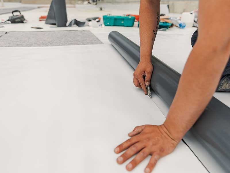 Close up of a worker cutting a piece off of a white TPO sheet on a commercial roof install